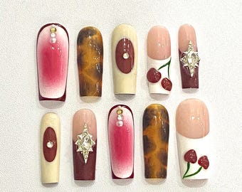 May include: Set of ten false nails with various designs. The designs include a red ombre, a cherry, a leopard print, a star, and a red circle.