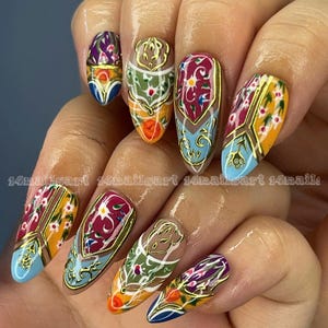 May include: A hand with long, almond-shaped nails, each adorned with intricate designs. The nails feature a gold outline with colorful patterns in shades of blue, orange, green, and purple. The text "14nailsart 14nailsart 14nails" is visible.