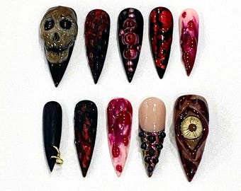 Puede incluir: Conjunto de diez uñas postizas con temática de Halloween con varios diseños, incluyendo una calavera, un ojo y patrones rojos y negros.