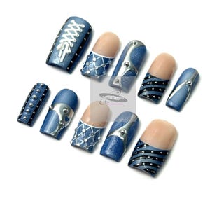 May include: A set of ten artificial nails with a denim design. The nails feature various embellishments, including silver-colored metal accents, white lace-up details, and black and silver stripes. Some nails have a natural-toned base.