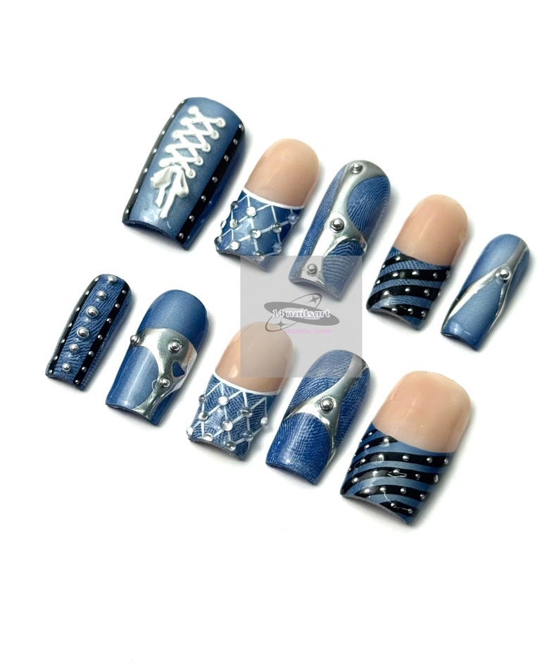 May include: A set of ten artificial nails with a denim design. The nails feature various embellishments, including silver-colored metal accents, white lace-up details, and black and silver stripes. Some nails have a natural-toned base.