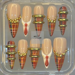 May include: A set of ten artificial nails in a clear plastic case. The nails feature a nude base with various designs, including plaid patterns, gold accents, and miniature tie details. The nails are designed to be long and pointed.