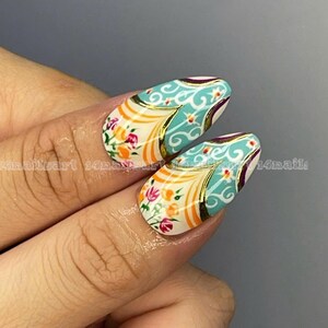 May include: Two almond-shaped nails with intricate designs. The nails feature a white base with floral and ornamental patterns in orange, pink, teal, and gold. The text "14nailart 14nails" is visible on the left and right sides of the image.