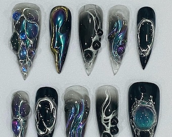 Puede incluir: Diez uñas postizas de stiletto negras y plateadas con varios diseños iridiscentes y negros. Algunas uñas presentan un diseño de telaraña negro y blanco, otras tienen un diseño de remolino negro e iridiscente, y algunas tienen un diseño de cara negro e iridiscente.