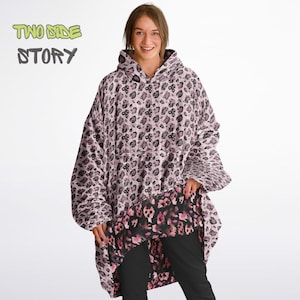 Pode incluir: Um moletom com capuz de tamanho grande com um capuz grande, com estampa de leopardo rosa e preto. O moletom tem um bolso na frente e é feito de um material macio e felpudo. O texto "TWO SIDE STORY" está escrito em verde e preto sobre um fundo branco.