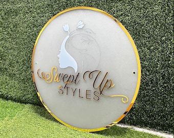 May include: A white circular sign with a gold border. The sign has a stylized image of a woman's face with hair and a flower on top of her head. The text "Swept Up Styles" is written in a cursive font below the image.