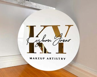Może przedstawiać: Okrągły biały znak z złotymi literami "KY" i tekstem "Makeup Artistry" poniżej. Imię "Kezban Yasar" jest napisane czarnym pismem odręcznym poniżej liter.