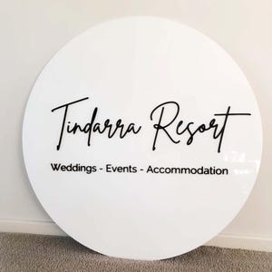 Op de afbeelding: Rond wit bord met zwarte tekst die "Tindarra Resort" en "Weddings - Events - Accommodation" luidt.