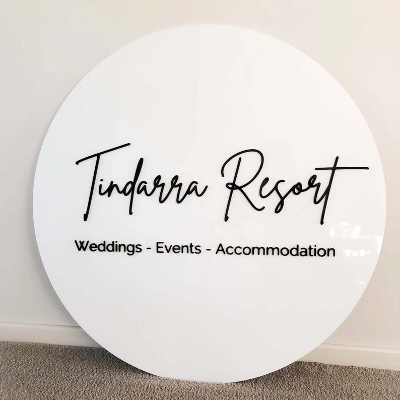 Op de afbeelding: Rond wit bord met zwarte tekst die "Tindarra Resort" en "Weddings - Events - Accommodation" luidt.