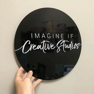 Op de afbeelding: Zwart rond bord met witte tekst die "Imagine If Creative Studios" luidt.