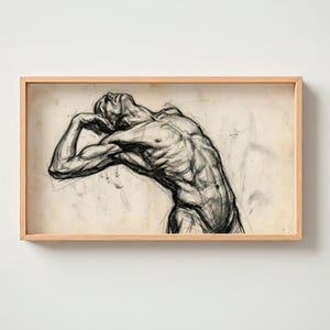 Könnte beinhalten: Gerahmte Bleistiftskizze einer muskulösen Figur in einer Pose der Kontemplation oder Anstrengung. Das Kunstwerk, in Grautönen gehalten, ist vor einem beigen Hintergrund platziert und in einem hellen Holzrahmen eingefasst. Die Form der Figur ist detailliert, wobei die Anatomie betont wird.