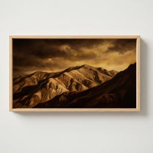 Puede incluir: Un cuadro de paisaje rectangular en un marco de madera clara que representa una cordillera bajo un cielo oscuro y tormentoso. La escena presenta tonos marrones profundos y ocre dorado, resaltando la textura rugosa de los picos.