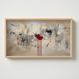 Puede incluir: Pintura abstracta en un marco de madera clara. La obra presenta un fondo texturizado con bloques beige, blancos y grises. Una salpicadura roja central con pintura goteando es el punto focal, con líneas negras que irradian hacia afuera.