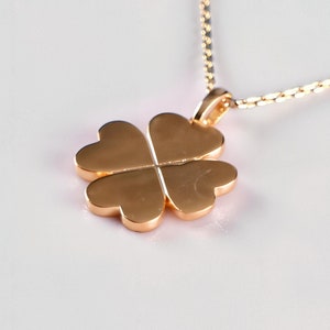 May include: A gold-colored necklace with a four-leaf clover pendant. The pendant is a solid, heart-shaped design. The chain is delicate and thin, and the necklace is displayed on a white background.