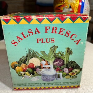 May include: A vintage Salsa Fresca Plus food processor box. The box is teal with red, yellow, and green geometric patterns. The words "SALSA FRESCA PLUS" are prominently displayed. An illustration of fresh vegetables and the food processor is featured.