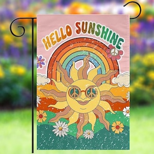 May include: A pink garden flag with a rainbow, a sun with peace sign sunglasses, and the text "Hello Sunshine".