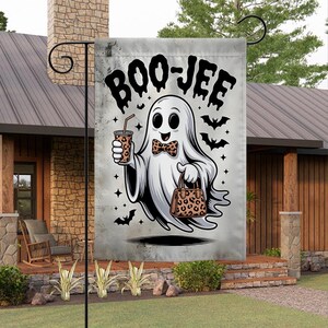 May include: A Halloween garden flag featuring a cartoon ghost holding a drink and a purse with a leopard print design. The flag has the text "BOO-JEE" in large, black letters, with bats and stars around the ghost.