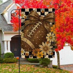 May include: A decorative garden flag featuring a football design with a large bow and floral accents. The football is brown with white stitching, surrounded by daisies in shades of yellow and cream, set against a black and white checkered background.