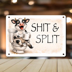 May include: A rectangular metal sign with a cartoon cow sitting on a toilet, holding a roll of toilet paper. The sign has the words "SHIT & SPLIT" in black text.
