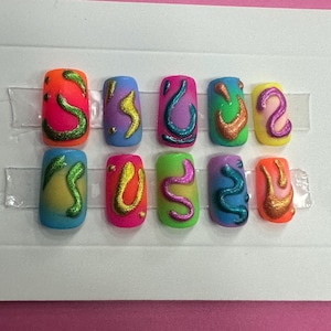 May include: Set of ten colorful fake nails with abstract designs. Each nail is a different color with a swirl design in a contrasting color. The nails are arranged in two rows of five on a white background.