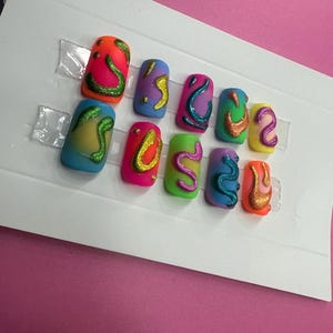 May include: Set of eight colorful fake nails with abstract designs. The nails are decorated with swirls and lines in various colors, including green, yellow, orange, pink, and blue.
