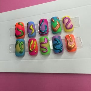 May include: Set of ten colorful fake nails with abstract designs. The nails are painted in various colors, including blue, green, yellow, orange, and pink. Each nail has a different abstract design, such as swirls, lines, and dots. The nails are arranged in two rows of five.