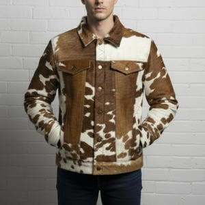May include: A brown and white cowhide jacket with a classic collar, two chest pockets, and button closures. The jacket features a unique pattern and is made of a textured material. The model is wearing dark blue jeans.