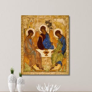 May include: A rectangular wall art print featuring a reproduction of the Holy Trinity icon. The artwork displays three figures with halos seated around a table with a central chalice, rendered in shades of gold, blue, and brown on a textured background.