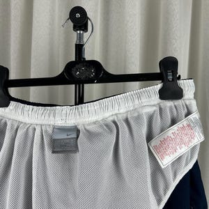 Puede incluir: Pantalones cortos deportivos azul marino con forro de malla blanco. Los pantalones cortos cuelgan de una percha negra. Se ve una peque&ntilde;a etiqueta Nike. Tambi&eacute;n hay una etiqueta blanca con texto rojo.