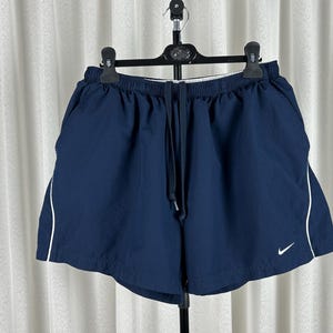 Puede incluir: Pantalones cortos deportivos azul marino con ribete blanco en los laterales. Los pantalones cortos tienen una cintura el&aacute;stica con cord&oacute;n y un peque&ntilde;o logotipo blanco de Nike en la pierna izquierda.