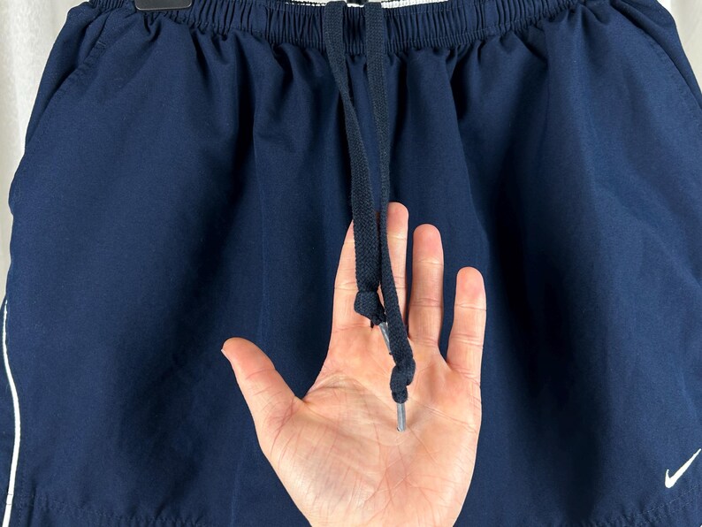 Puede incluir: Pantalones cortos deportivos azul marino con una raya blanca en el lateral y un cord&oacute;n. El logotipo de Nike es visible. Los pantalones cortos est&aacute;n hechos de un material ligero.