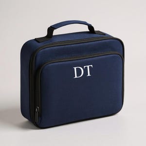 May include: A navy blue lunch bag with a black zip and handle. The bag features the white initials "DT" on the front. The rectangular bag has a small pocket on the front.