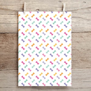 May include: A white sheet of paper with a repeating pattern of colorful bone shapes. The bones are in shades of orange, pink, purple, and green.
