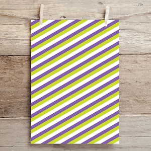 May include: A rectangular sheet of paper with a diagonal striped pattern. The stripes alternate between white, lime green, and purple. The paper is held by a wooden clothespin attached to a string, against a wooden background.