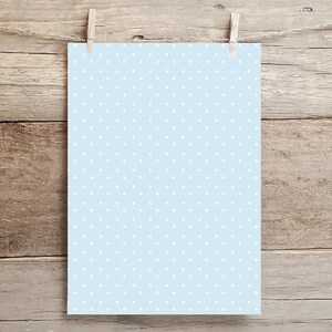 May include: A light blue sheet of paper with a white polka dot pattern. The paper is hanging from two clothespins on a wooden background.