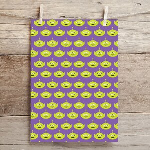 May include: Purple wrapping paper with a repeating pattern of green alien heads with three eyes. The aliens are smiling.