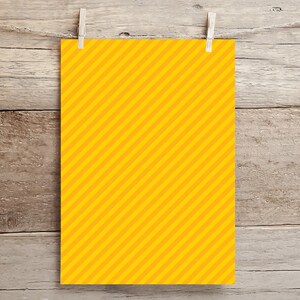 May include: A yellow sheet of paper with diagonal orange stripes hanging on a wooden background with clothespins.