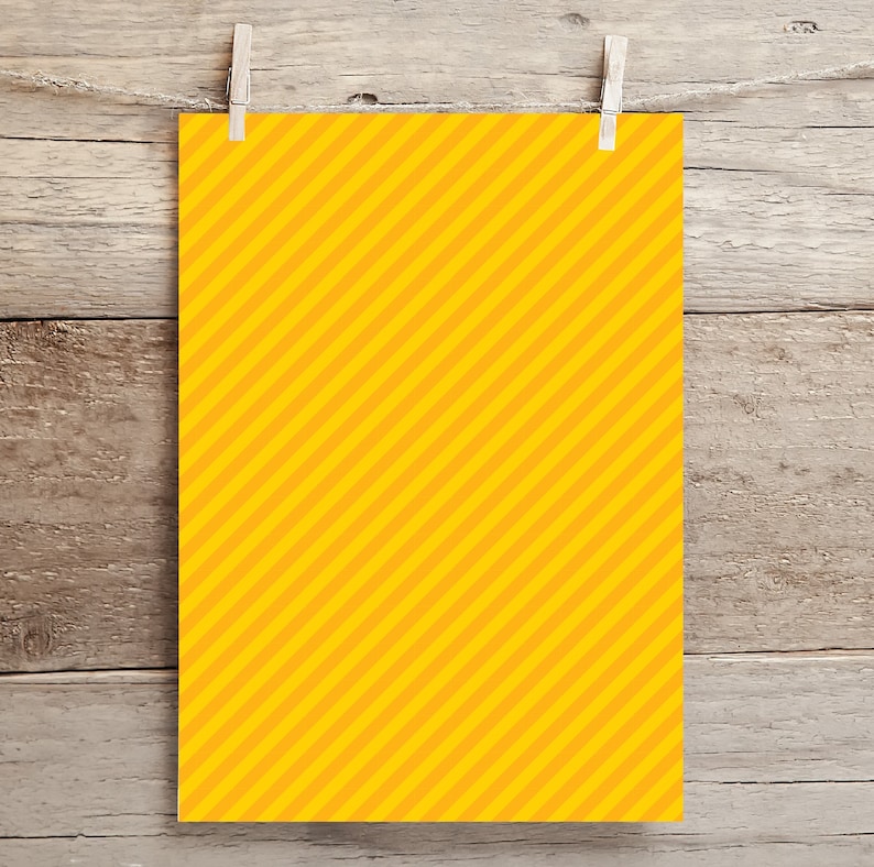 May include: A yellow sheet of paper with diagonal orange stripes hanging on a wooden background with clothespins.