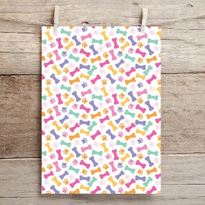 May include: A white background with a repeating pattern of colorful dog bones and paw prints. The bones are in shades of orange, pink, purple, and green. The paw prints are orange.