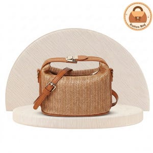 May include: A woven rattan handbag with a rectangular shape, featuring a top handle and a detachable shoulder strap. The bag has a brown leather trim and a silver-coloured clasp. The bag is displayed on a white surface.