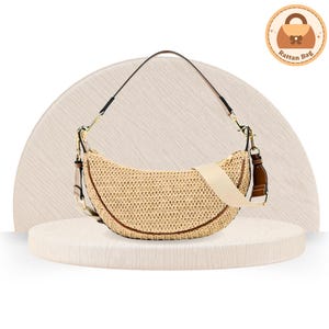 May include: A crescent-shaped rattan bag with a beige woven texture. It features a brown leather trim, a cream-colored shoulder strap, and a black and gold handle. The bag is displayed on a white platform.