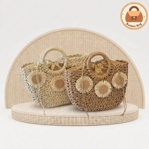 Puede incluir: Dos bolsos de mano de ratán tejido con detalles de girasoles. Uno es de color beige claro, el otro marrón. Ambos tienen asas redondas y cierres de cordón. Los bolsos se exhiben sobre una plataforma tejida de color claro.