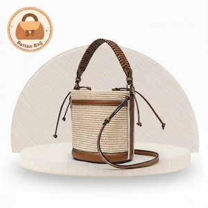 May include: A beige and brown rattan bucket bag with a braided handle and a detachable shoulder strap. The bag has a brown leather base and trim, with drawstring closures. The bag is displayed on a white surface.