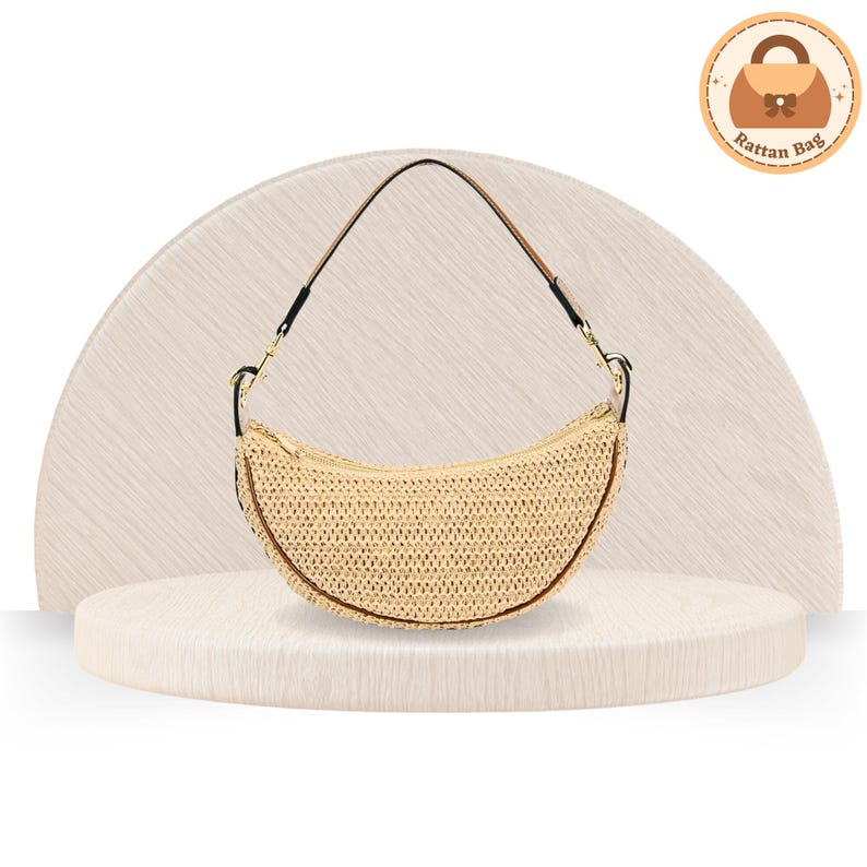 May include: A crescent-shaped rattan bag with a black strap and gold-colored hardware. The bag is made of woven beige material and has a brown trim. The bag is displayed on a light-colored, textured surface.