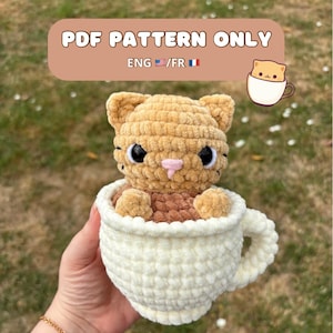 Peut inclure: Un chat en crochet dans une tasse blanche. Le chat est brun clair avec des yeux noirs et un nez rose. La tasse est de couleur crème. Le texte sur l'image indique "PDF PATTERN ONLY" et "ENG/FR".
