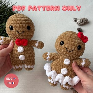 Peut inclure: Deux bonhommes en pain d'épices crochetés, l'un avec un nœud papillon rouge et l'autre avec un nœud rouge. Ils ont des yeux noirs, des accents blancs et le texte "PDF PATTERN ONLY" en rose.