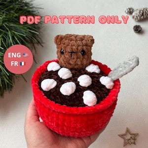 Peut inclure: Un ours en peluche au crochet émerge d'un bol rouge rempli de fil marron et de guimauves en fil blanc, avec une cuillère grise. Le bol a un bord rouge. Le texte "PDF PATTERN ONLY" est en haut. L'image comprend également les drapeaux des États-Unis et de la France.