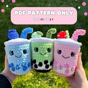 Peut inclure: Trois peluches amigurumi en crochet en forme de bubble tea. La première est bleue avec des perles de boba blanches et bleues, la deuxième est verte avec des perles de boba blanches et noires, et la troisième est rose avec des perles de boba blanches. Les peluches ont des visages souriants avec des yeux et des bouches noirs.  MODÈLE PDF UNIQUEMENT ANG/FR.