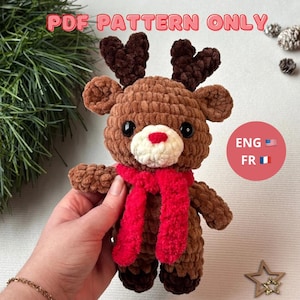 Peut inclure: Un renne au crochet marron fait à la main avec des bois marron foncé, un museau blanc avec un nez rouge et une écharpe rouge. Le texte "PDF PATTERN ONLY" est en haut. Un petit cercle montre les drapeaux des États-Unis et de la France.