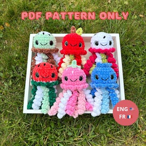 Peut inclure: Six méduses crochetées colorées, chacune avec un design unique et un visage souriant. Les méduses sont disposées dans un plateau blanc sur de l'herbe verte. Le texte "PDF PATTERN ONLY" est affiché au-dessus des jouets. Le texte "ENG FR" est également présent.